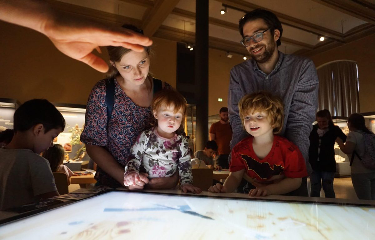 Besucher des Naturkundemuseums am interaktiven Multitouch Tisch mit optischer Objekterkennung